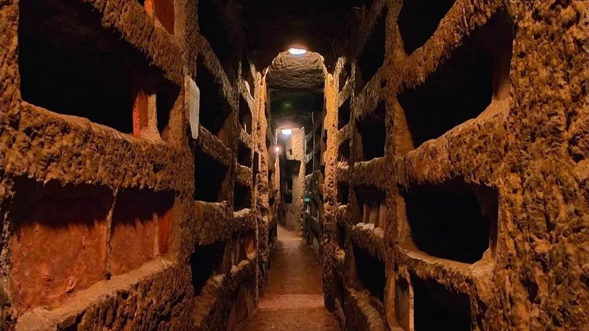 Small English-speaking group in a lamplit burial gallery on a Rome underground tour of the catacombs